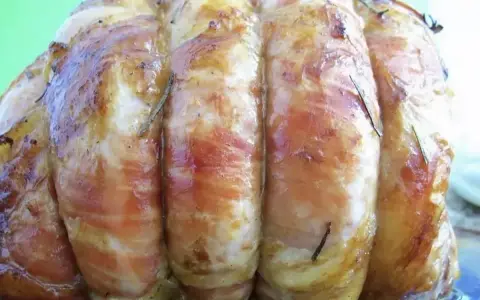 Un rôti de veau savoureux, enveloppé de lard et parsemé de romarin, prêt à être dégusté.