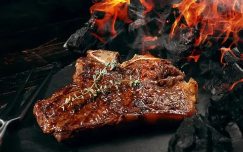 Un steak T-bone juteux, garni de thym, cuit sur des braises ardentes. Une parfaite recette barbecue pour les amateurs de viande.