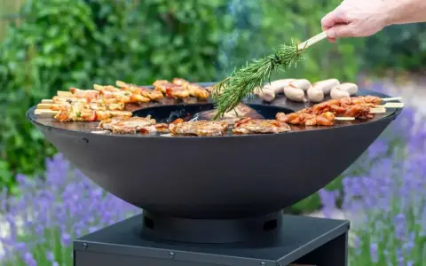 Un brasero moderne cuit brochettes et saucisses. On y voit comment fonctionne un brasero, avec une branche de romarin pour parfumer.