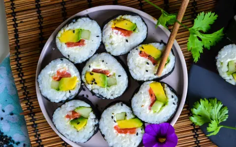 Assiette de makis frais, parfaits pour une recette sushi maison. Avocat, saumon et concombre roulés dans du riz et des algues, parsemés de graines de sésame.