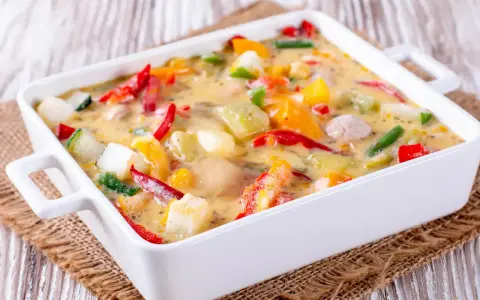 Un gratin de légumes coloré et crémeux, avec des poivrons, courgettes et autres légumes dans une sauce onctueuse, prêt à être dégusté.