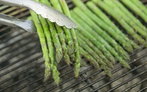 Des asperges vertes grillées, parfaites pour une recette simple et savoureuse. Les pinces saisissent un bouquet prêt à être retourné.