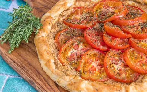 Une délicieuse tarte tomates aux herbes, sur une planche en bois, avec une branche de thym frais à côté.