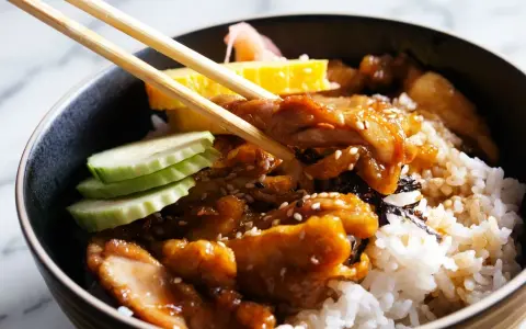 Un bol de riz garni de poulet teriyaki, de concombre, d'omelette et de gingembre mariné, prêt à être dégusté avec des baguettes.