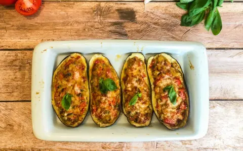 Quatre moitiés d'aubergines garnies de légumes et de fromage gratiné, décorées de feuilles de basilic frais.