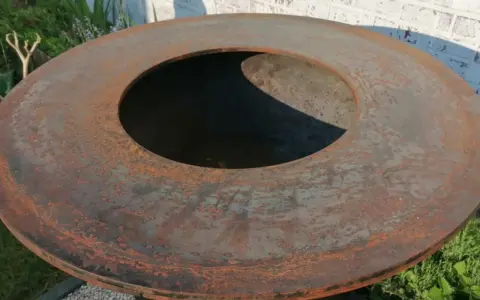 Gros plan sur le plateau rouillé d'un brasero, prêt pour son culottage. La surface métallique présente des nuances orangées et grises.