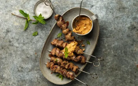 Brochettes d'agneau grillées au barbecue, servies avec une sauce aux arachides et garnies de menthe fraîche.