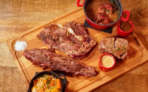 Assortiment de viande à griller, steak, et ragoût de bœuf, servi avec des sauces et des légumes sur une planche en bois.