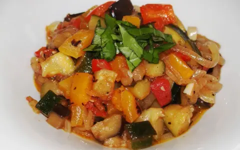 Un plat coloré de ratatouille recette, avec des dés de courgettes, aubergines, poivrons et tomates, garni de basilic frais.