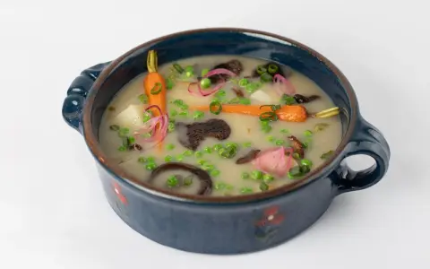 Délicieuse recette végétarienne : un potage crémeux aux carottes, petits pois, pommes de terre et champignons, garni d'oignons rouges et de ciboule.
