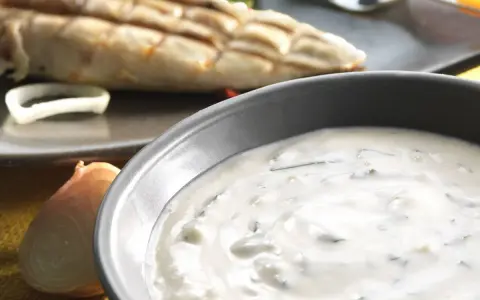 Sauce blanche crémeuse avec herbes, peut-être une différence sauce tartare et béarnaise. Poisson grillé en arrière-plan.