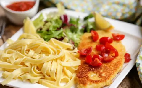 Une assiette de pâtes fraîches, une escalope milanaise dorée garnie de tomates cerises, et une salade verte. Un délice !