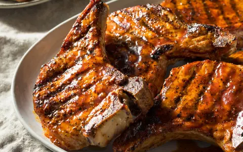 Trois côtes de porc barbecue, grillées et nappées d'une sauce savoureuse, sur une assiette blanche.