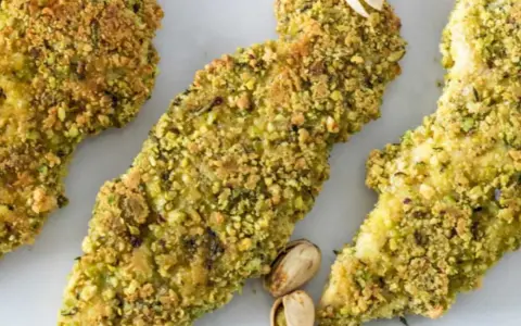 Trois tendres morceaux de poulet pistache, croustillants et dorés, sont présentés sur fond blanc.
