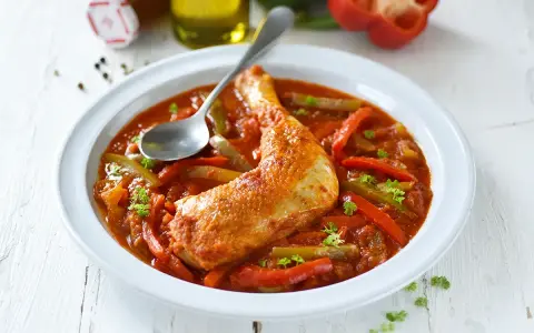 Un plat de poulet basquaise savoureux, avec un morceau de poulet doré dans une sauce tomate riche aux poivrons rouges et verts, garni de persil frais.