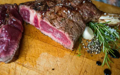 Un succulent côte de bœuf barbecue, saignant et parsemé de gros sel, est prêt à être dégusté. Accompagné de romarin frais, d'ail et de poivre concassé.