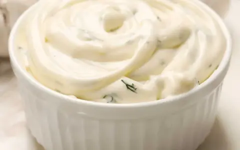 Un bol blanc rempli de sauce césar crémeuse, parsemée d'herbes vertes. Parfait pour accompagner une salade.