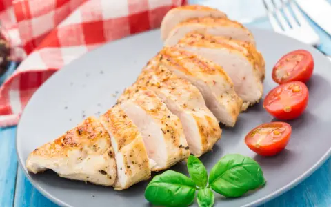 Un délicieux filet de poulet grillé, tranché et servi avec des tomates cerises et du basilic frais sur une assiette grise.