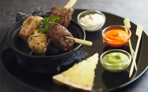 Brochettes de poulet et de bœuf, accompagnées de différentes sauces : mayonnaise, sauce tomate épicée et sauce verte.
