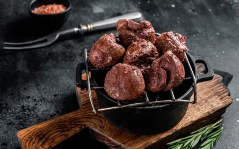 Un plat de rognons de veau grillés, servis dans une cocotte en fonte sur une planche en bois, avec une pincée de sel rose et une branche de romarin.