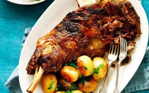 Épaule d'agneau rôtie, servie avec des pommes de terre et du persil. Le temps de cuisson de l'épaule d'agneau au barbecue Weber est parfait pour cette viande tendre.