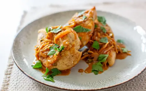 Trois escalopes de poulet nappées d'une sauce onctueuse aux oignons caramélisés et garnies de persil frais. Un plat savoureux et réconfortant.