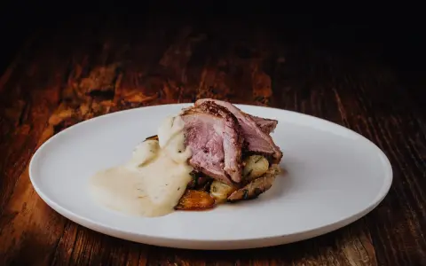 Tranches de gigot d'agneau rosées, nappées d'une sauce chasseur onctueuse, servies sur des pommes de terre rôties. Un délice pour les gourmands.