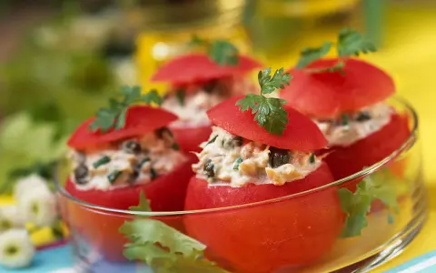Tomates farcies froides aux légumes, garnies de persil frais, présentées dans un bol en verre. Un délice estival.