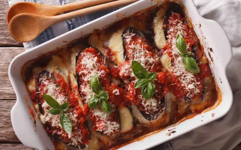 Aubergine parmigiana gratinée, garnie de sauce tomate, fromage fondant et basilic frais. Un délice italien prêt à être dégusté.