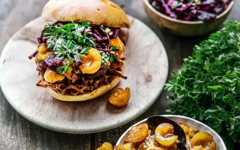 Un délicieux burger de pulled pork garni de fruits et de persil frais, accompagné d'une salade de chou rouge et de fruits confits.