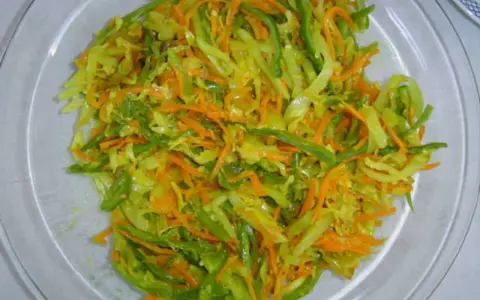 Un plat coloré d'achard de légumes, mêlant carottes râpées, chou et poivrons verts, prêt à être dégusté.