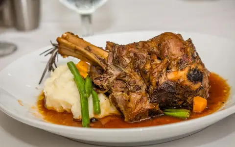 Une souris d'agneau braisée, servie avec une purée onctueuse, des haricots verts croquants et des dés de carottes, le tout nappé d'une sauce savoureuse.