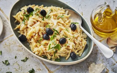 Un plat de bacalhau à brás, effiloché et garni d'olives noires et de persil frais. Une touche d'huile d'olive et d'ail est visible à côté.