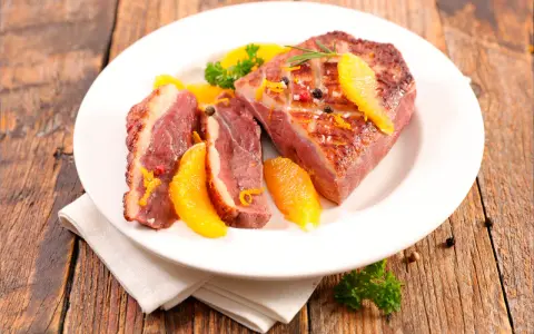 Magret de canard tranché, garni d'orange et de romarin, prêt à être dégusté. Une excellente recette plancha pour un repas savoureux.