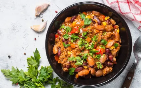 Un bol de chili sin carne, garni de persil frais, avec des haricots rouges, du maïs et des poivrons. Parfait pour un repas réconfortant.