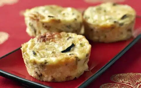 Trois petits flans de courgettes dorés et appétissants sur une assiette rouge, parfaits pour un repas léger.
