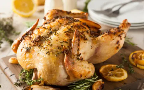 Un délicieux poulet rôti, doré et parfumé aux herbes, est servi sur une planche en bois avec des quartiers de citron et de l'ail rôti.