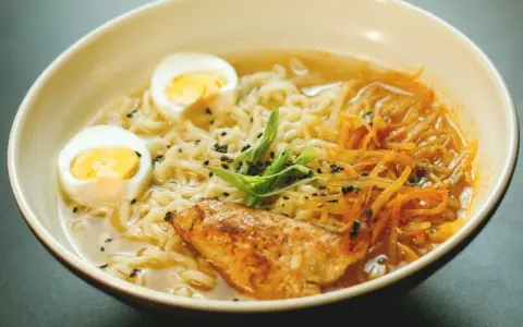 Un bol de ramen poulet avec nouilles, œuf dur, poulet grillé, julienne de carottes et oignons verts. Une recette réconfortante.