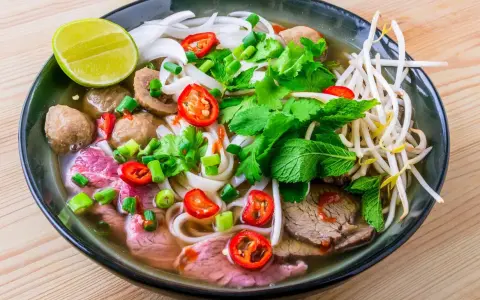 Un bol de soupe pho savoureux avec du bœuf, des boulettes, des nouilles, des herbes fraîches, des piments et un quartier de citron vert.