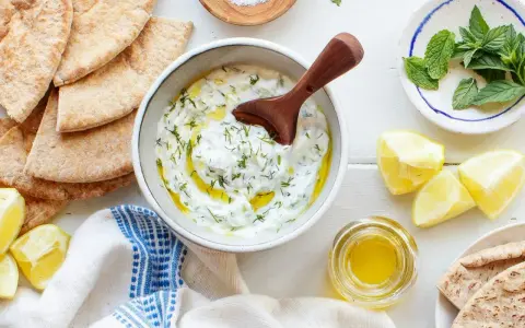 Un bol de tzatziki crémeux, garni d'aneth et d'huile d'olive, prêt à être dégusté avec du pain pita. Une recette fraîche et savoureuse.