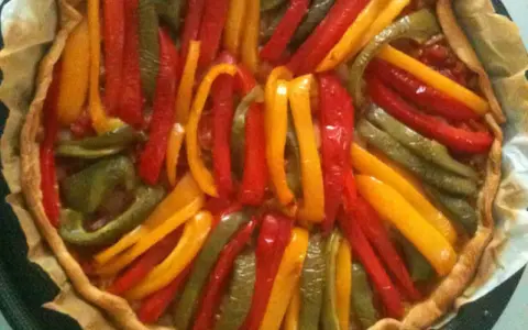 Tarte aux poivrons colorés, un délice visuel et gustatif. Les lanières de poivrons rouges, jaunes et verts forment un motif rayonnant sur la pâte dorée.