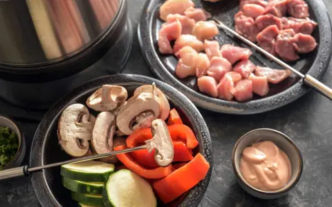 Préparation d'une fondue bourguignonne 3 viandes : cubes de poulet et bœuf crus, champignons, courgettes, poivrons et sauce.