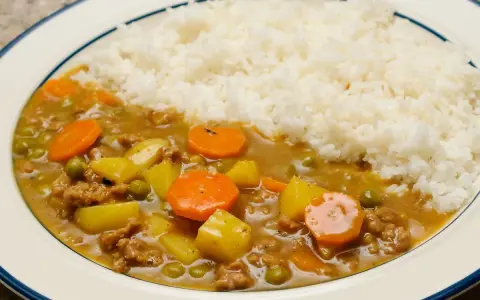Un plat de riz blanc servi avec un curry japonais savoureux, garni de morceaux de carottes, de pommes de terre et de petits pois.