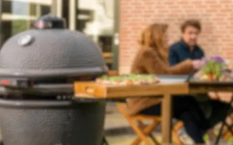 Un couple profite d'un repas en plein air avec une pizza fraîchement préparée, la cuisson kamado promettant une saveur incomparable.