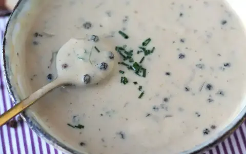 Une cuillère dorée plonge dans une onctueuse sauce au poivre, garnie de ciboulette fraîche.
