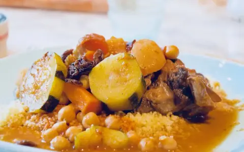 Un plat généreux de couscous algérien, garni de légumes tendres, de pois chiches et de morceaux de viande savoureux, le tout nappé d'une sauce parfumée.