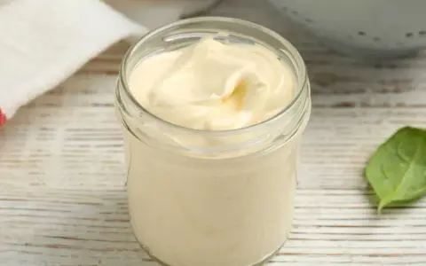 Un pot de mayonnaise sans huile, crémeuse et onctueuse, sur une table en bois. Une feuille verte à côté.