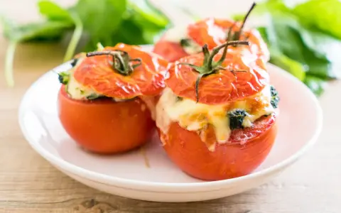 Trois tomates farcies au fromage fondant et aux herbes, servies sur une assiette blanche.