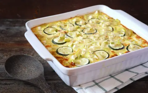 Un gratin de courgettes à l'ancienne, doré et crémeux, garni de rondelles de courgettes et de poireaux, prêt à être dégusté.