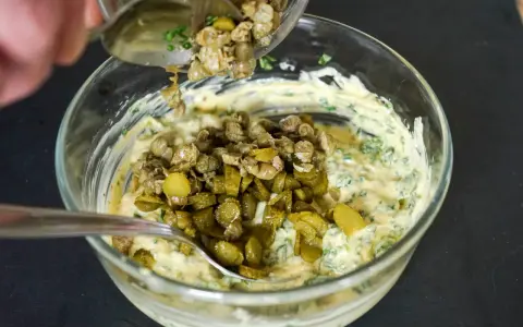 Ajout de câpres et cornichons hachés à une base crémeuse pour préparer une sauce gribiche savoureuse.